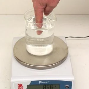 A finger dipped into a beaker of water on a digital scale